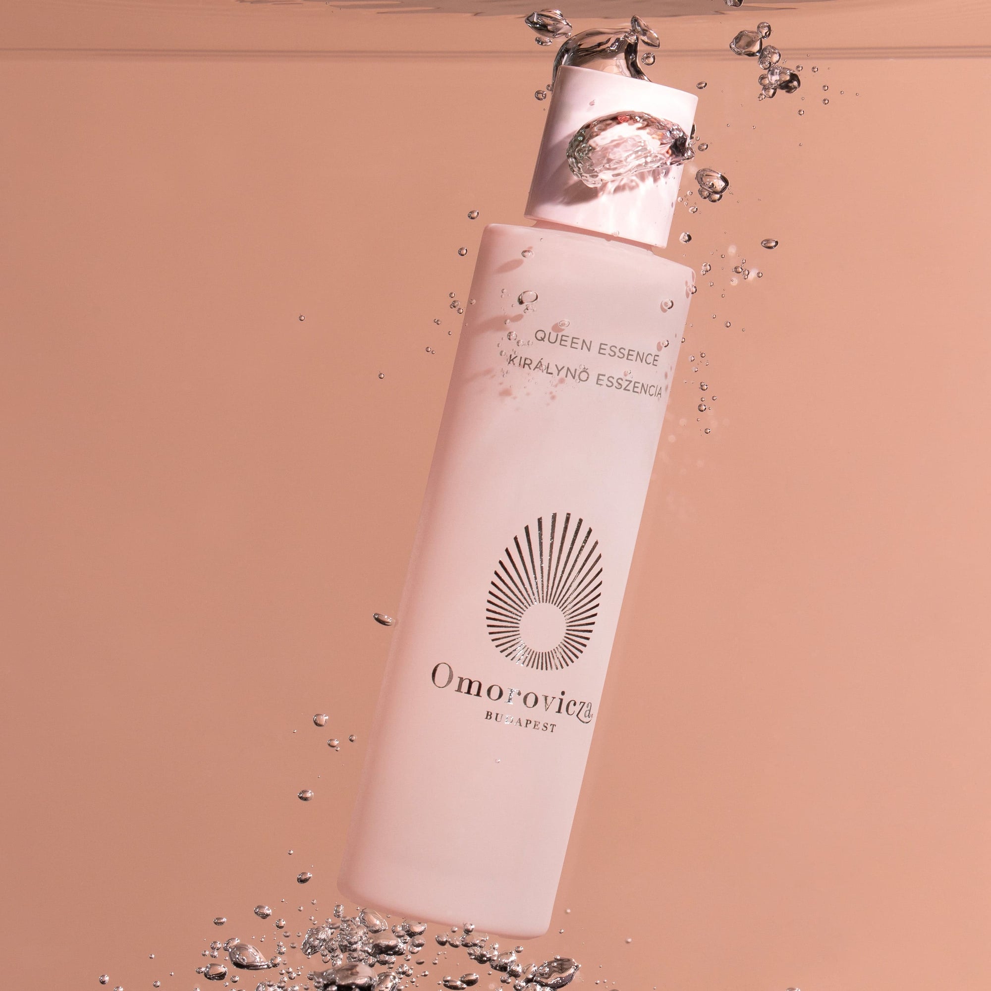 A tall bottle of the Queen Essence on the pink background, Submerged into water. 