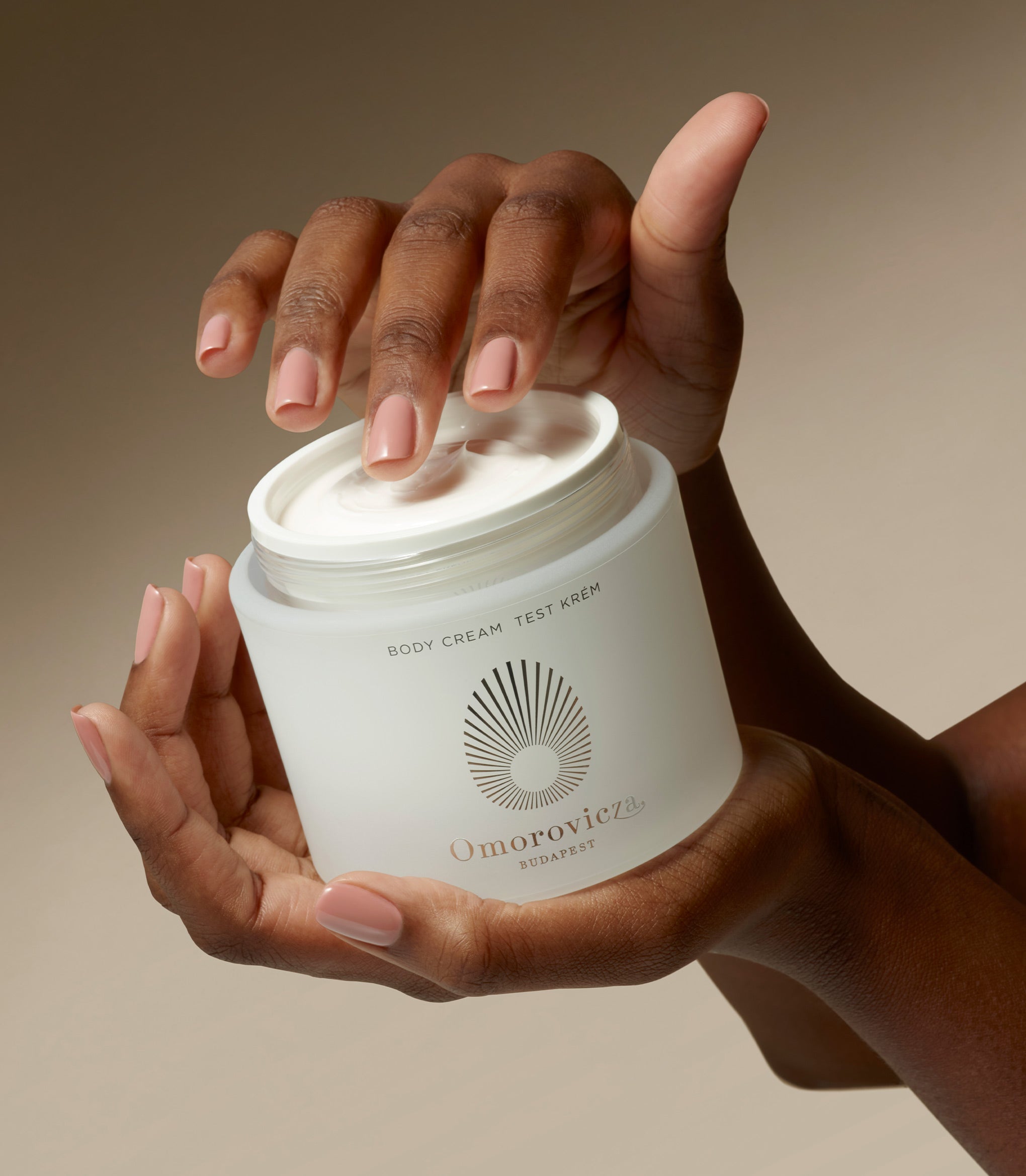 Hands are holding a jar of Omorovicza Body cream.