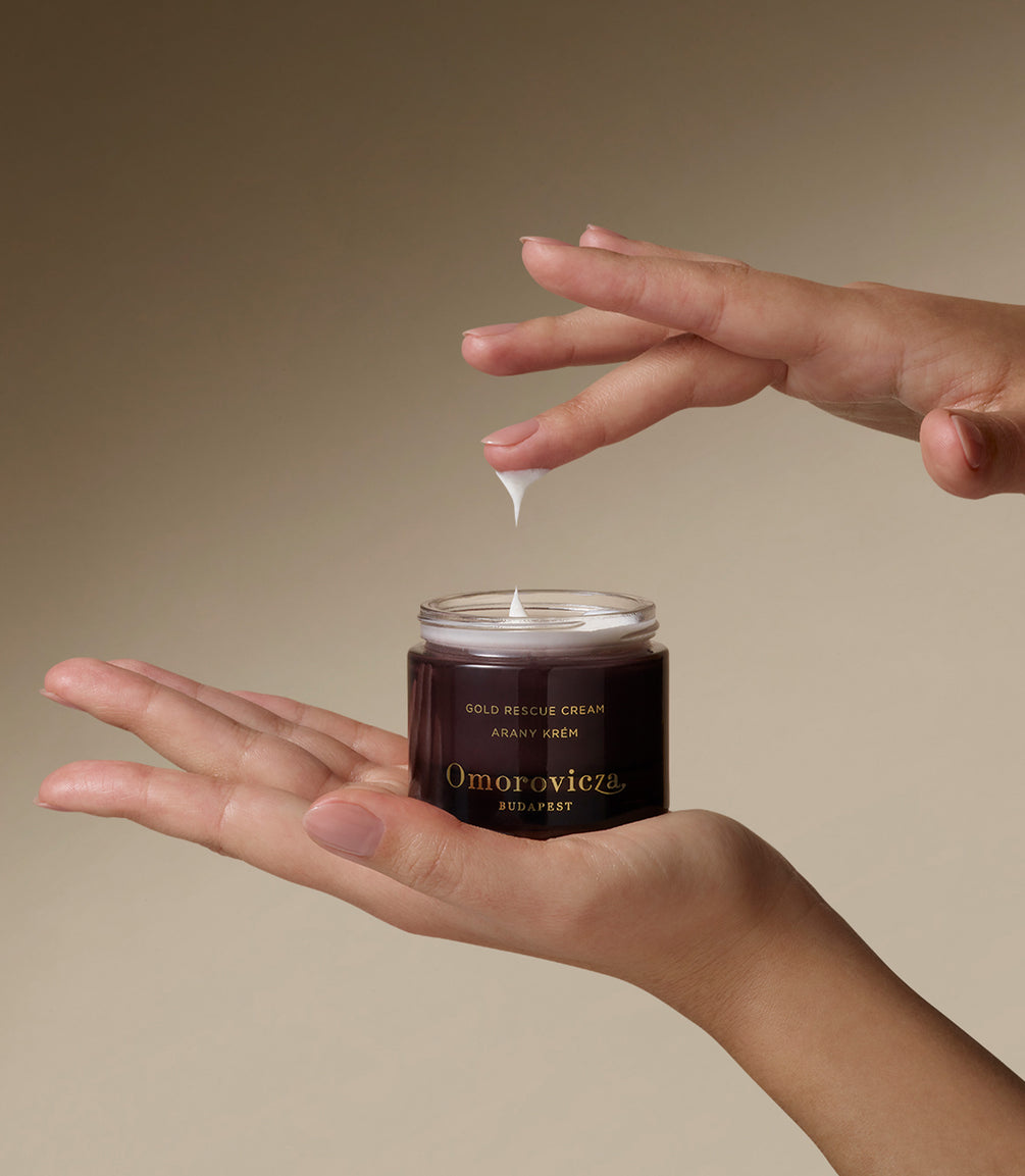Hands holding Gold Rescue Cream. Picking up a little bit of product with a finger.